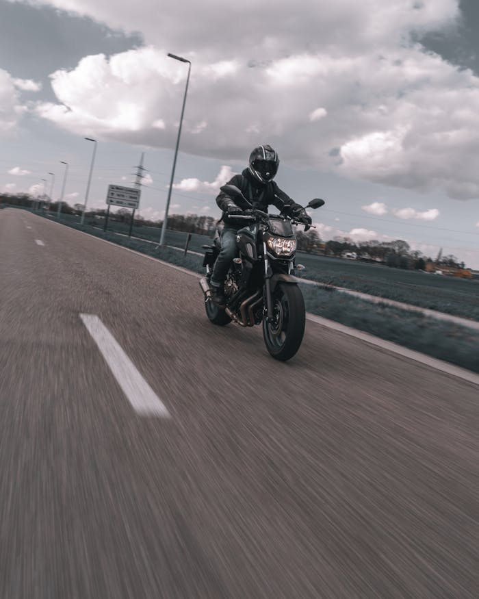 Motorcyclist speeds down a clear road under a cloudy sky, capturing adventure and freedom.