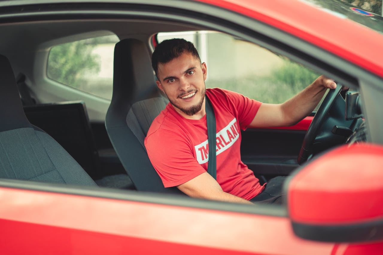 Smiling man driving a red car while wearing a seatbelt, showcasing safety and joy.